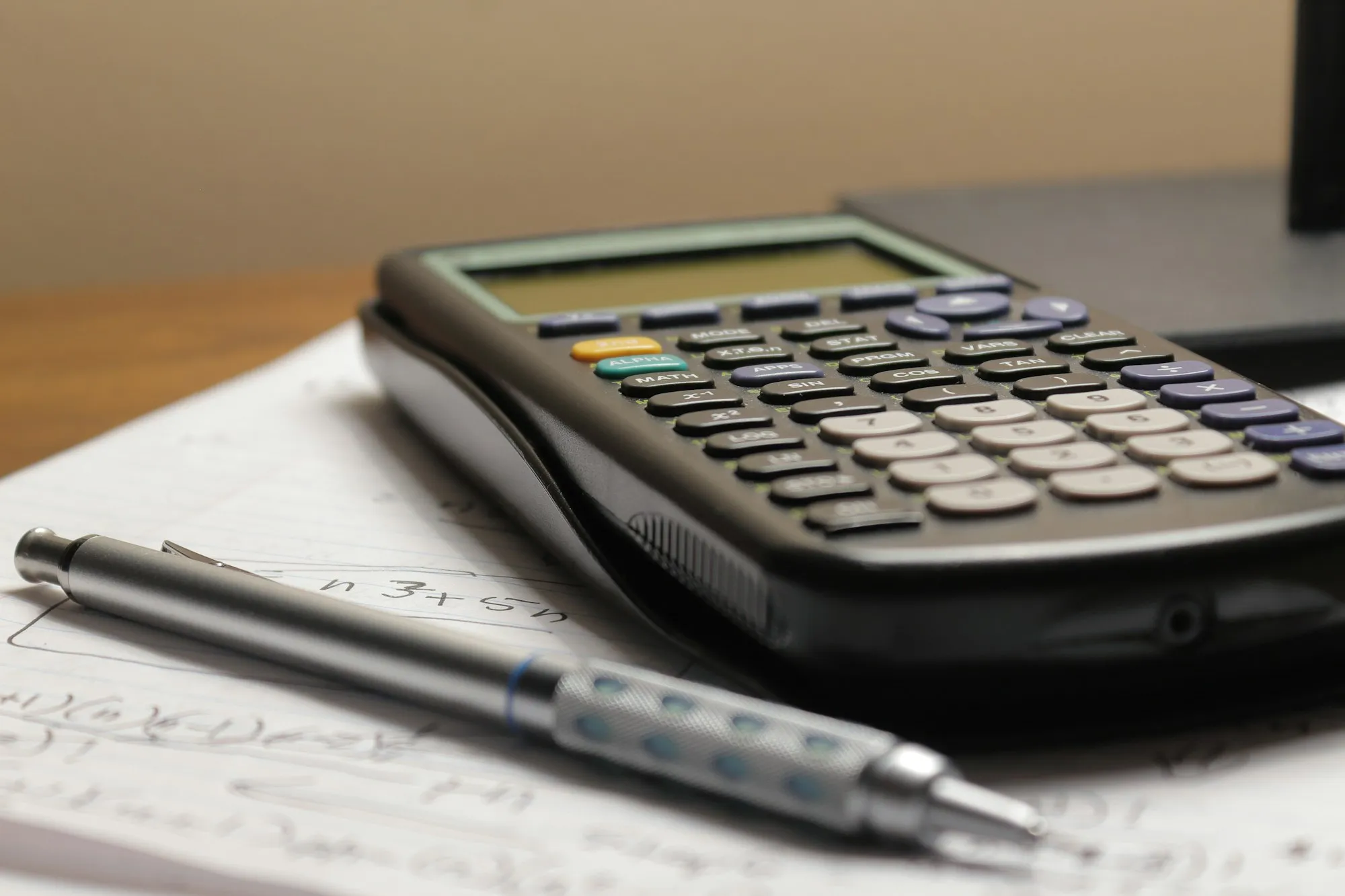 A calculator and a pen lying on a sheet covered in calculations