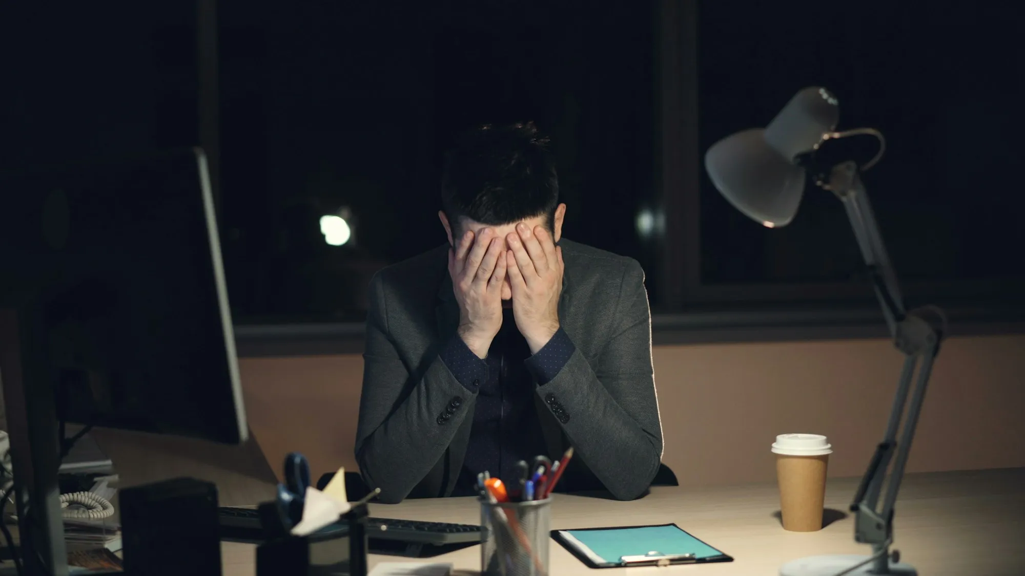 A trader alone at his desk at night, head in his hands after a loss